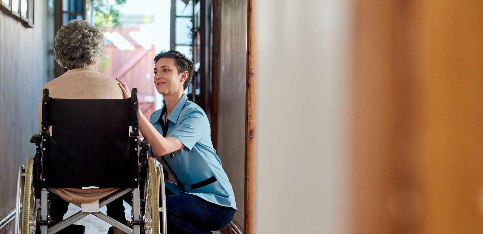 An older lady in a wheelchair with a support worker kneeling down next to her