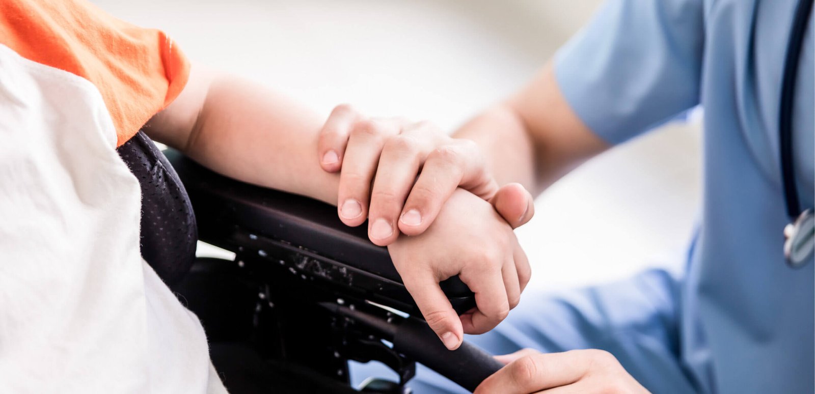Child in wheelchair. Healthcare working resting their hand on child's wrist.