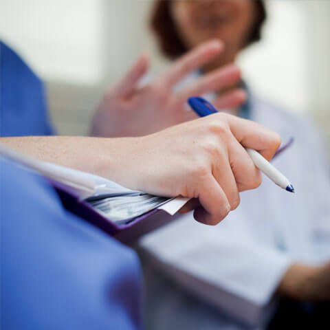 Health care worker with a clipboard and pen talking with other healthcare professionals