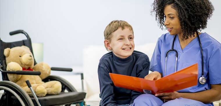 Health worker holding folder sitting next to a child with a wheelchair and teddy in the background