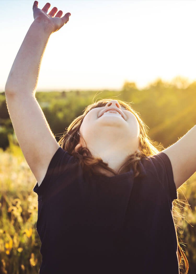 Child with arms in the air and sunsetting in the background